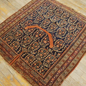 Navy floral patterned rug featuring a prominent orange crescent shape on distressed light wood floorboards.