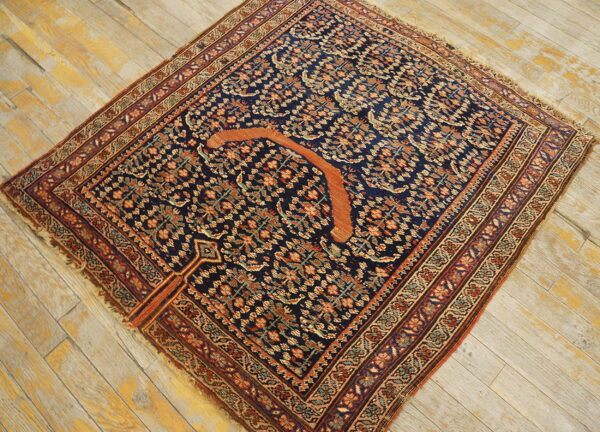 Navy floral patterned rug featuring a prominent orange crescent shape on distressed light wood floorboards.