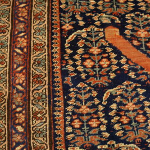 Close-up of a traditional navy and rust rug with a complex geometric border on light wood plank flooring.