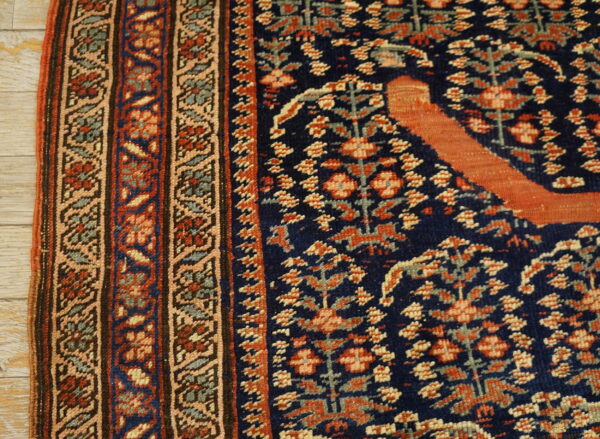 Close-up of a traditional navy and rust rug with a complex geometric border on light wood plank flooring.