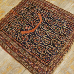 Dark blue rug featuring an intricate all-over pattern and a central rust-colored curved element on plank flooring.