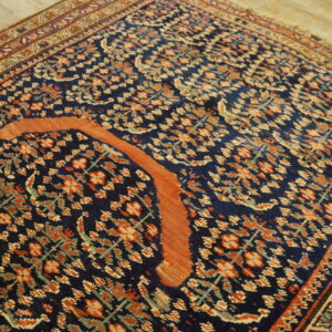 Traditional navy rug with dense orange and cream patterns, featuring a wide curved orange design element on wood flooring.