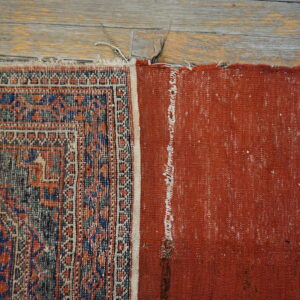 Geometric patterned rug edge and solid red backing resting on rustic distressed wood planks.