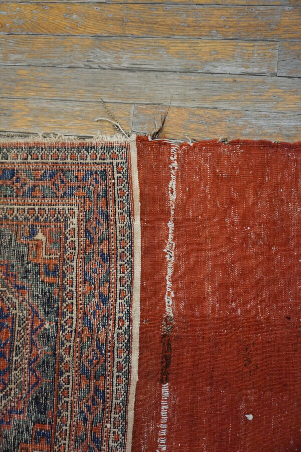 Geometric patterned rug edge and solid red backing resting on rustic distressed wood planks.