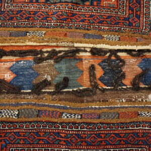 Geometric red and blue pile rug bordering bands of flatweave, thick brown texture, and shaggy dark yarn.