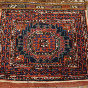 Small red and blue low-pile geometric rug with multiple borders displayed on weathered wood planks.