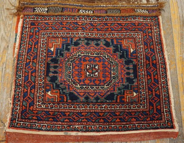 Small red and blue low-pile geometric rug with multiple borders displayed on weathered wood planks.