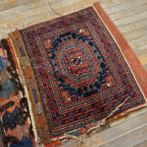 Geometric red, navy, and teal rug with rustic shaggy elements lying on distressed light wood floors.