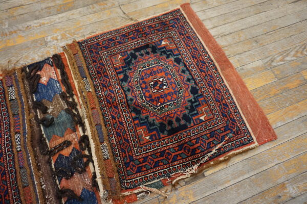 Geometric red, navy, and teal rug with rustic shaggy elements lying on distressed light wood floors.