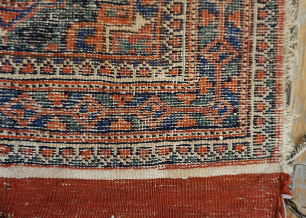 A close-up reveals the rug's geometric border in rust, blue, and cream above a flat woven end finish.