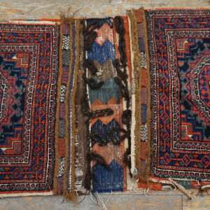 Two geometric red and navy piled rug panels connected by a colorful, textured flatweave band on wood flooring.