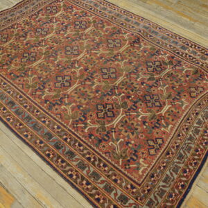 A rust red rug with a dense geometric pattern in blue, green, and tan rests on weathered wood planks.