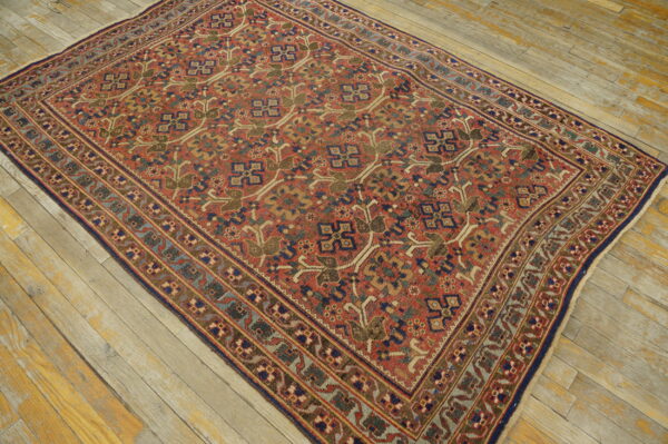 A rust red rug with a dense geometric pattern in blue, green, and tan rests on weathered wood planks.