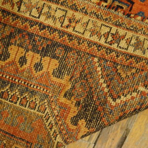 Close-up of a dense, low-pile rug featuring geometric patterns in orange, gold, and dark blue on wood floors.