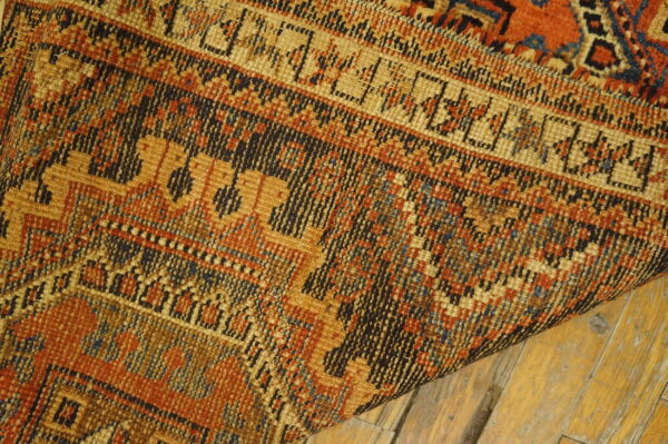 Close-up of a dense, low-pile rug featuring geometric patterns in orange, gold, and dark blue on wood floors.