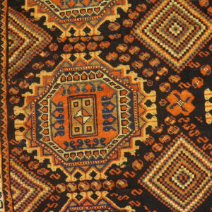 Geometric rug with intricate orange, navy, and tan patterns on a black field, resting on light wood flooring.