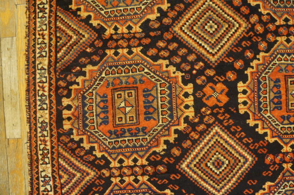 Geometric rug with intricate orange, navy, and tan patterns on a black field, resting on light wood flooring.