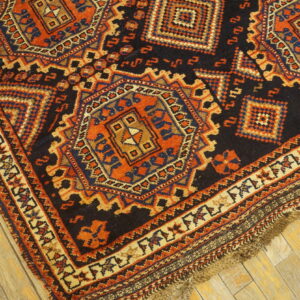 Corner view of a dark geometric rug with orange and blue medallions laid on light wooden floorboards.