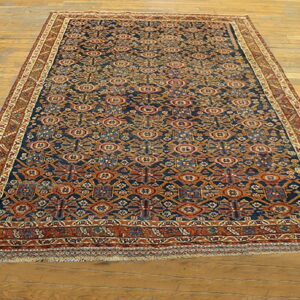 Low-pile rug with a detailed navy blue and rust geometric design displayed on light wooden plank flooring.