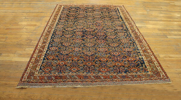 Low-pile rug with a detailed navy blue and rust geometric design displayed on light wooden plank flooring.