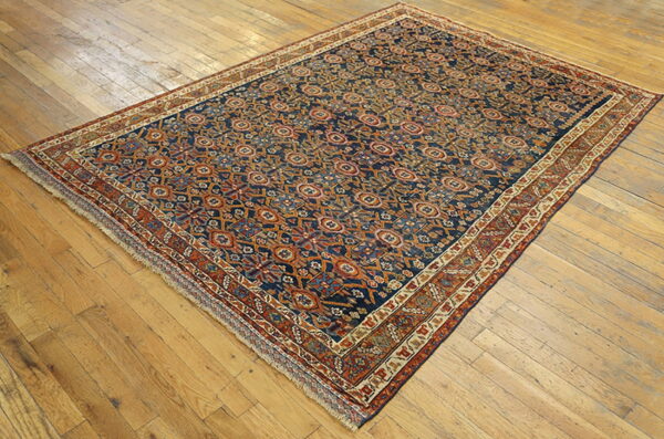 Navy blue area rug with detailed orange and rust geometric motifs on light brown hardwood flooring.
