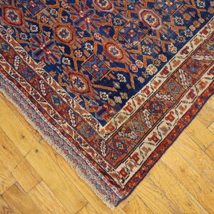 Close-up of a blue and orange geometric patterned rug corner on distressed light wood floors.