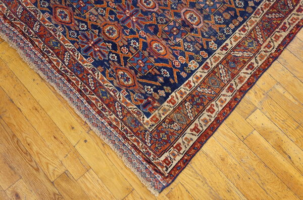 Close-up of a blue and orange geometric patterned rug corner on distressed light wood floors.