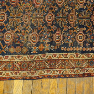 Detailed navy rug with geometric motifs in orange, blue, and tan rests on distressed wood flooring.