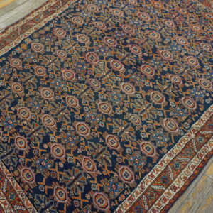 Dark blue rug with a dense orange, pink, and blue geometric pattern rests on weathered light wood floors.