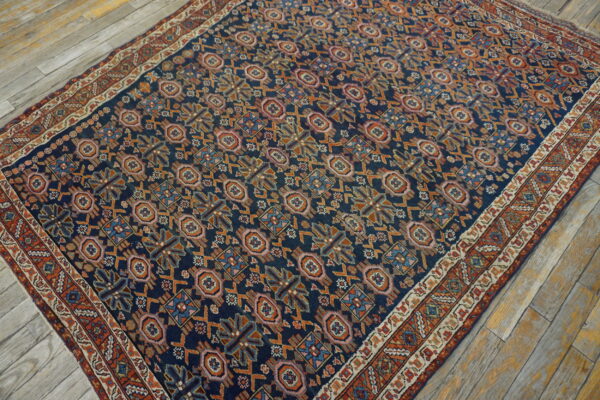 Dark blue rug with a dense orange, pink, and blue geometric pattern rests on weathered light wood floors.