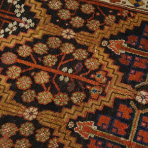 Detailed view of a low-pile rug featuring red, green, gold, and black tribal and stylized floral motifs.