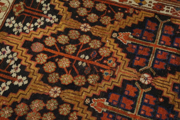 Detailed view of a low-pile rug featuring red, green, gold, and black tribal and stylized floral motifs.