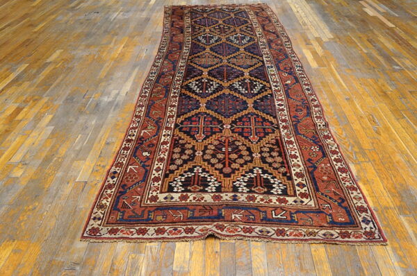 Traditional geometric runner rug in dark blue, rust, and gold on a distressed wood plank floor.