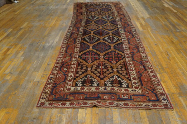 Dark blue and rust tribal runner rug with geometric patterns lies on worn golden wood flooring.