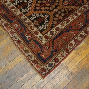 Rust, black, and navy patterned low-pile rug corner rests on yellow and gray weathered hardwood flooring.