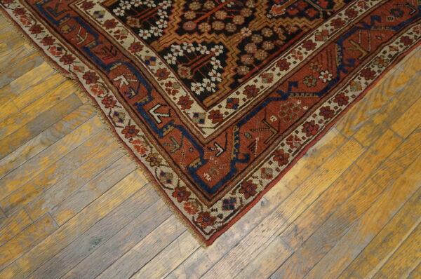 Rust, black, and navy patterned low-pile rug corner rests on yellow and gray weathered hardwood flooring.