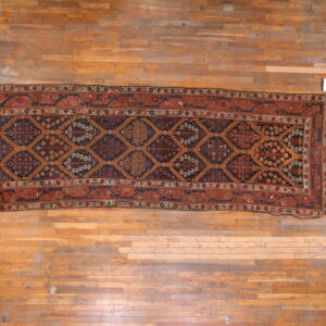 Geometric runner rug in dark blue, rust red, and tan colors centered on narrow plank hardwood flooring.