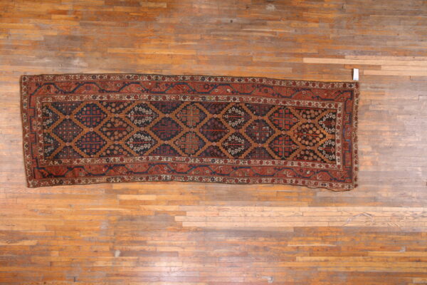 Geometric runner rug in dark blue, rust red, and tan colors centered on narrow plank hardwood flooring.