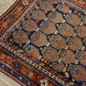 Navy field rug with repeating burnt orange tribal motifs and complex borders on light wood flooring.