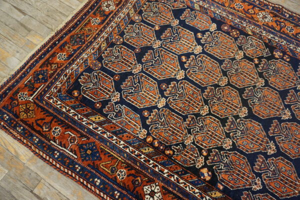 Navy field rug with repeating burnt orange tribal motifs and complex borders on light wood flooring.