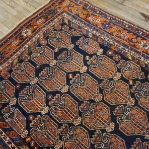 Low pile rug in navy blue and rust with repeating geometric motifs, shown on light wood flooring.