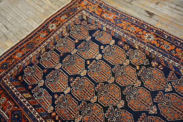Low pile rug in navy blue and rust with repeating geometric motifs, shown on light wood flooring.