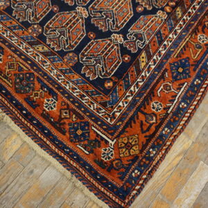 Corner view of a traditional navy and terracotta rug with complex geometric patterns on worn wood flooring.