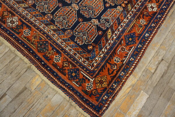 Corner view of a traditional navy and terracotta rug with complex geometric patterns on worn wood flooring.