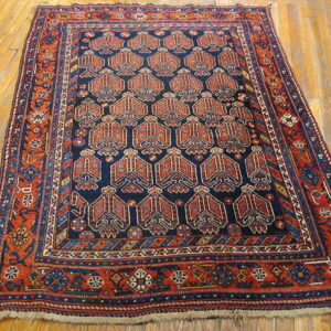 Dark blue rug with repeating rust-colored geometric motifs and complex borders, shown on plank wood flooring.