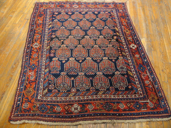 Dark blue rug with repeating rust-colored geometric motifs and complex borders, shown on plank wood flooring.