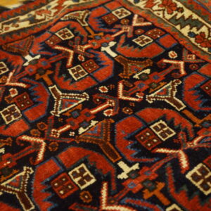 Red and navy geometric rug close-up shows detailed motifs and a cream border on wood flooring.