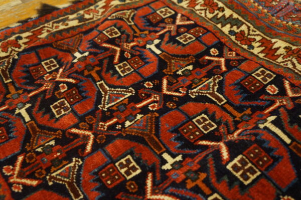Red and navy geometric rug close-up shows detailed motifs and a cream border on wood flooring.