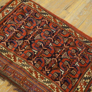 A small rug with red, navy, and cream geometric designs rests on distressed blonde wood flooring.