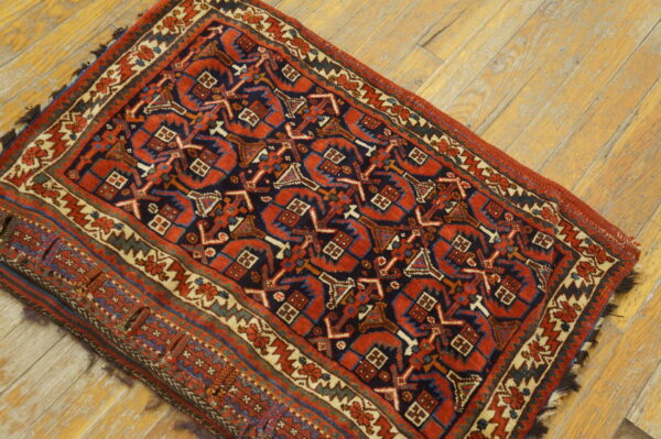 A small rug with red, navy, and cream geometric designs rests on distressed blonde wood flooring.